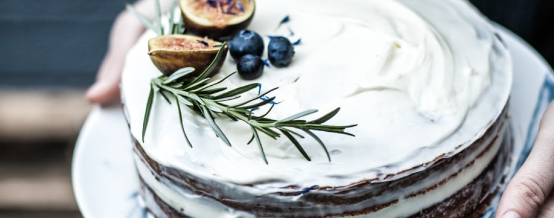 A rustic cake with white frosting and blueberries, rosemary and a fig for decoration